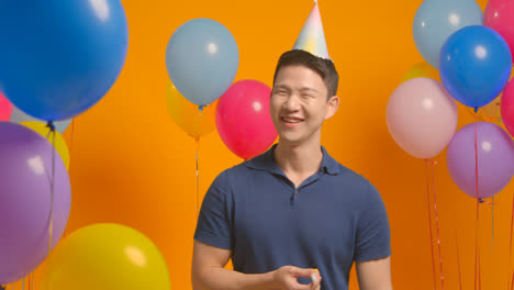 Studioporträt-Eines-Mannes-Mit-Partyhut,-Der-Geburtstag-Mit-Luftballons-Und-Partygebläse-Feiert